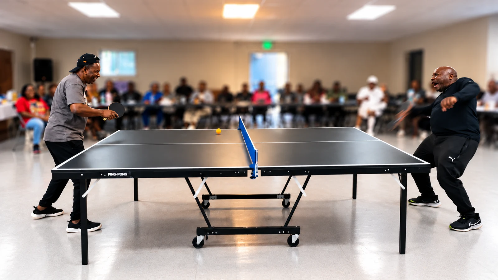 Two people playing table tennis at a fellowship gathering, with the audience softly blurred in the background